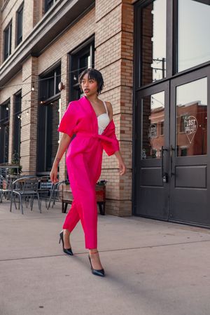 Dynamic fashion sequence in bright pink dress against urban brick building.