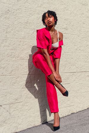 Fashion model poses dynamically in bright red outfit against white wall showing movement and style.
