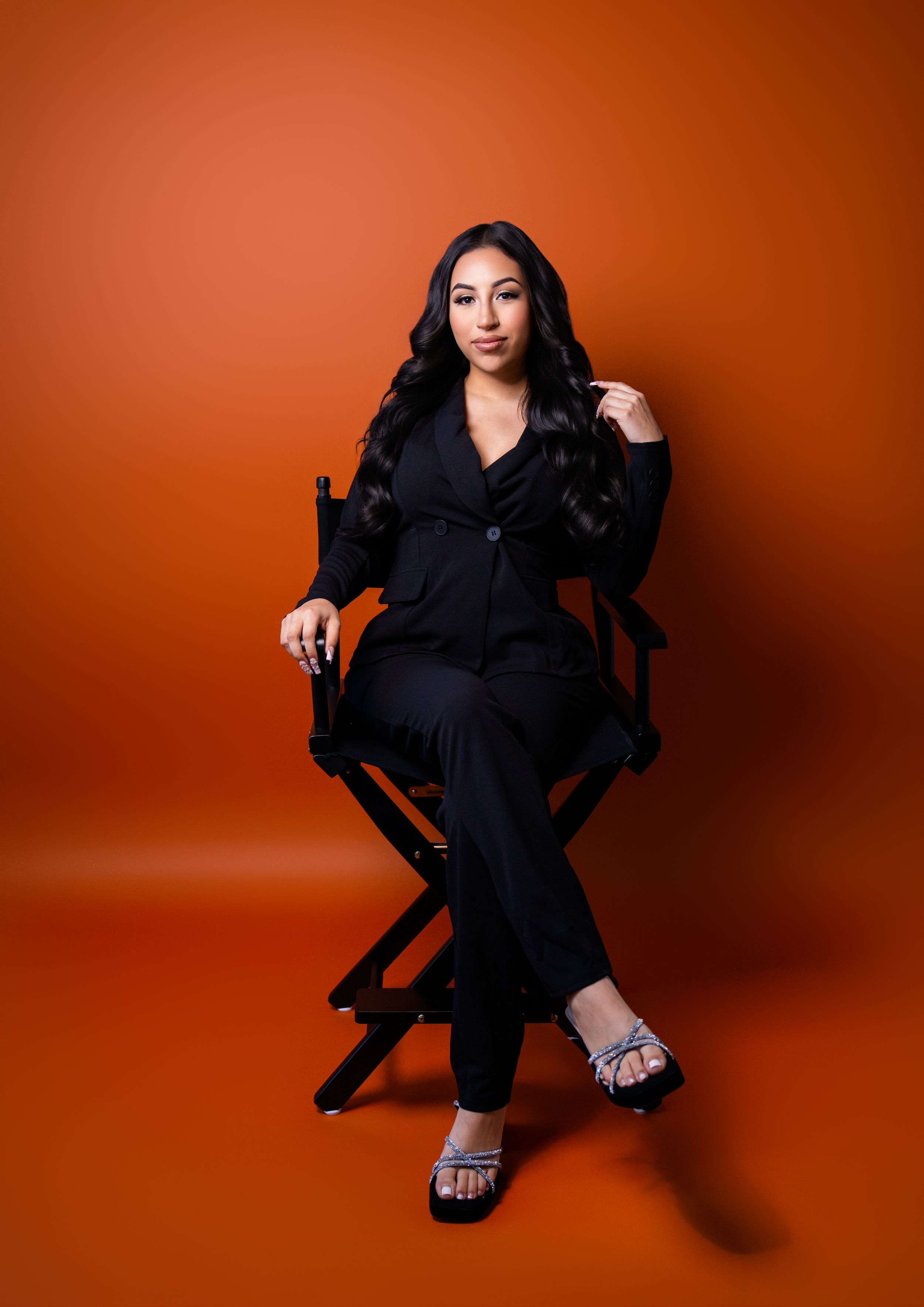 Fashion portrait series against vibrant orange background wearing black outfit.