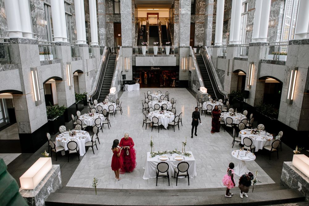 An elegant dining hall with tall white columns, multiple round tables with white tablecloths, and classic architectural details.