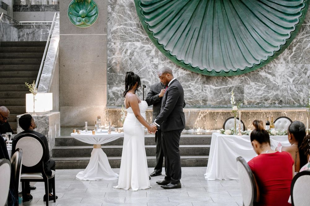 Wedding ceremony taking place in an elegant venue with large windows and teal decor accents.
