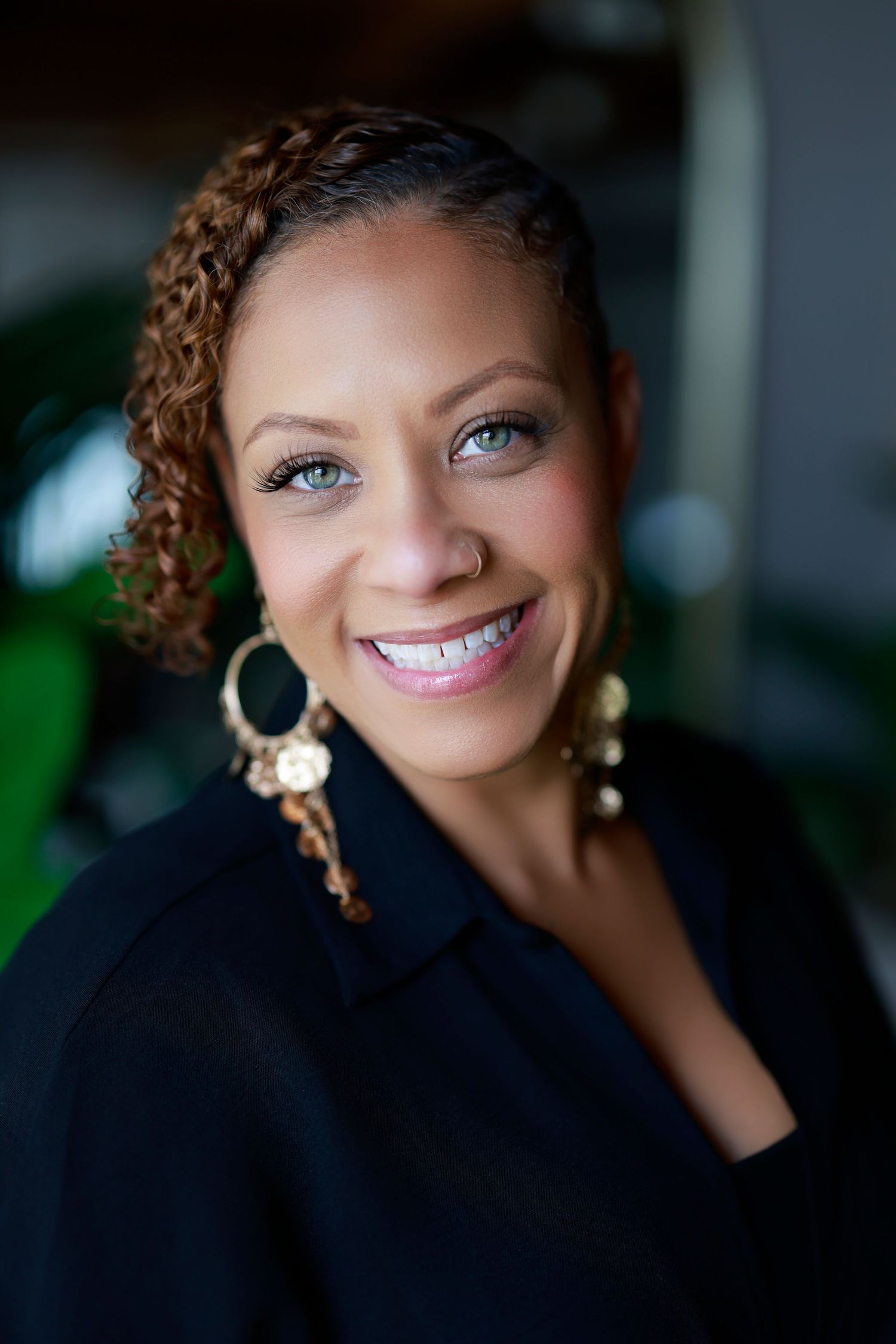Portrait of person with curly hair and bright smile wearing navy top against dark background.