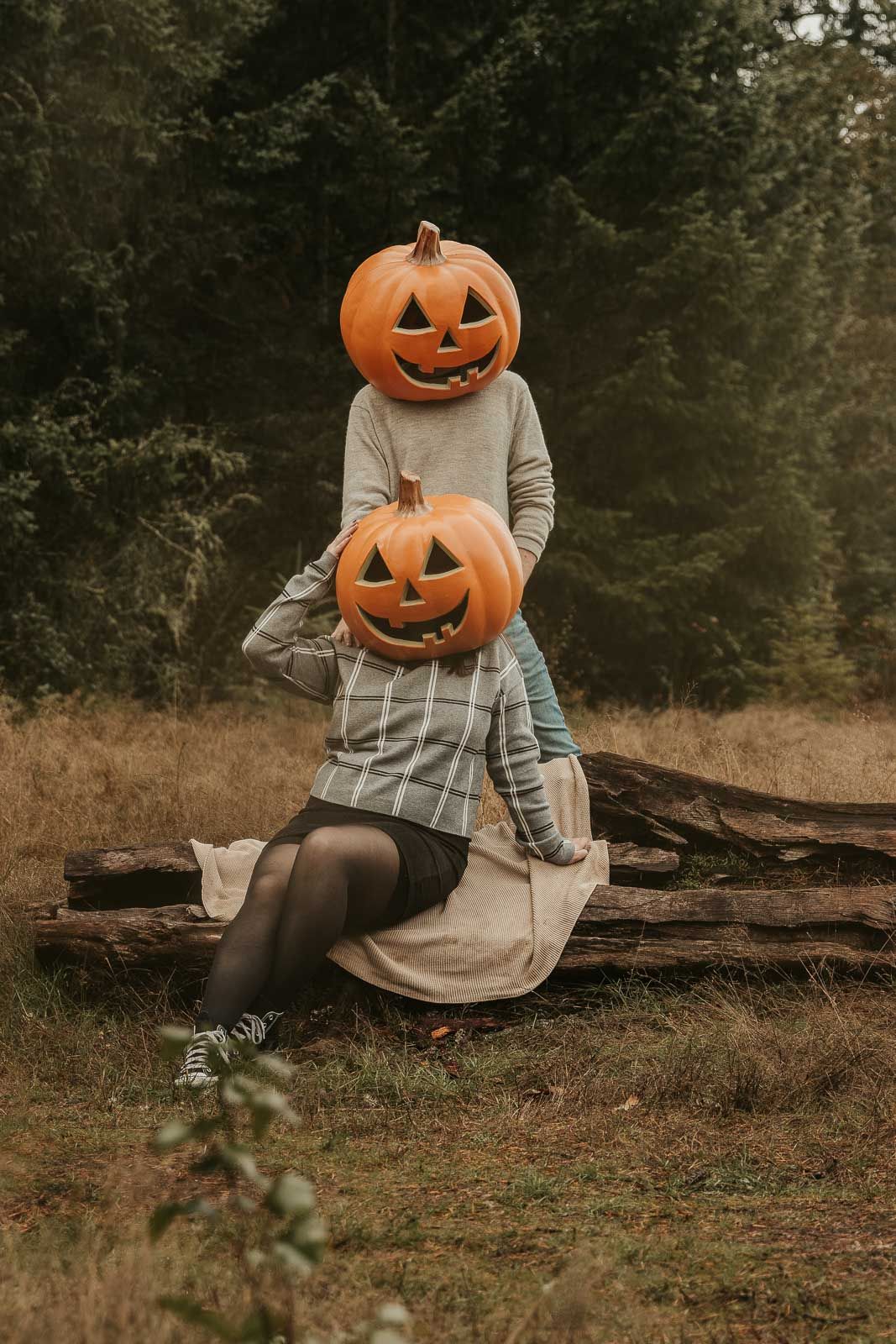 spooky Halloween couples photo shoot man and woman with pumpkin heads in open field with tall pine trees in background, spokane photography
