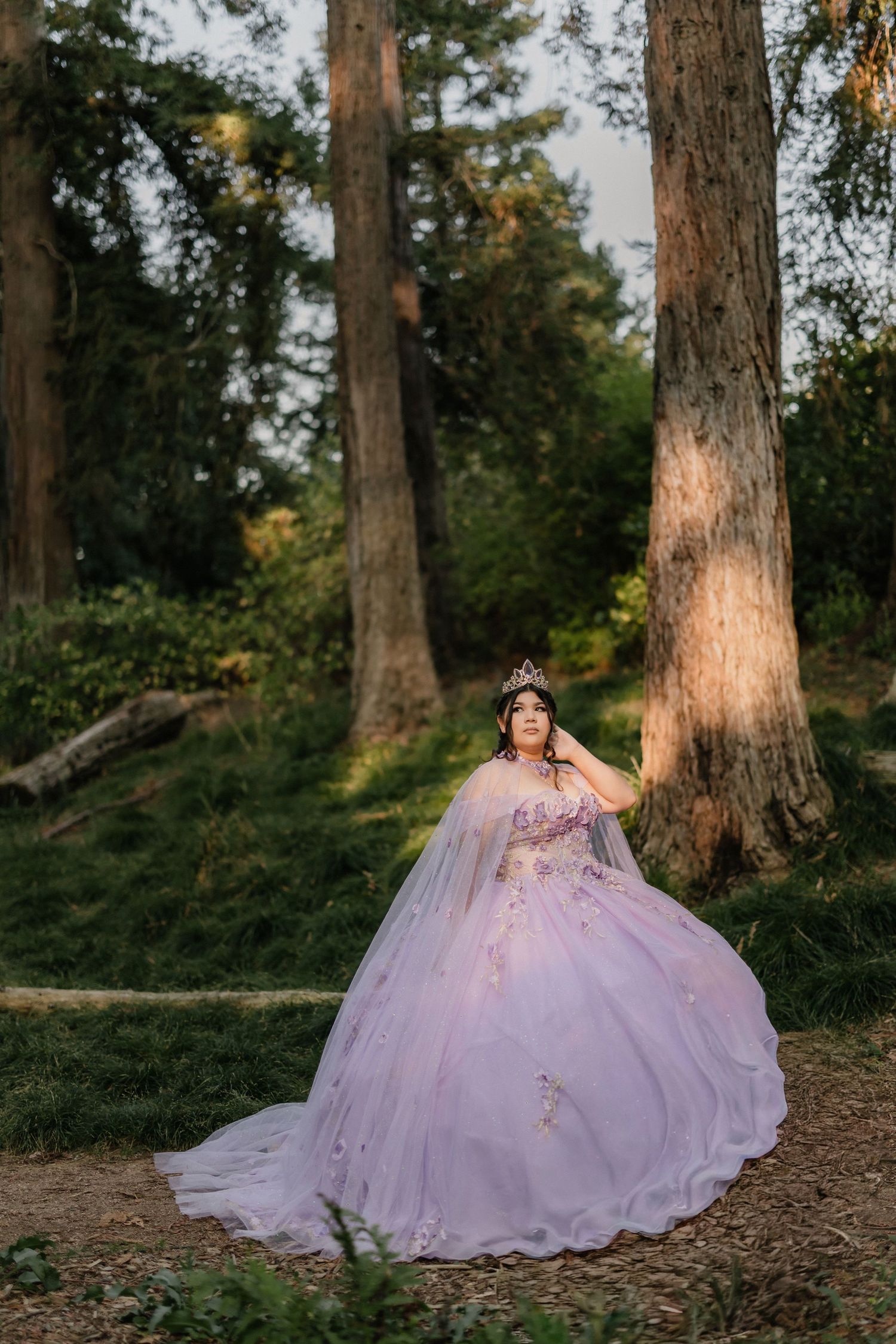 A dreamy forest portrait features a lavender ballgown-clad figure surrounded by towering trees at golden hour.