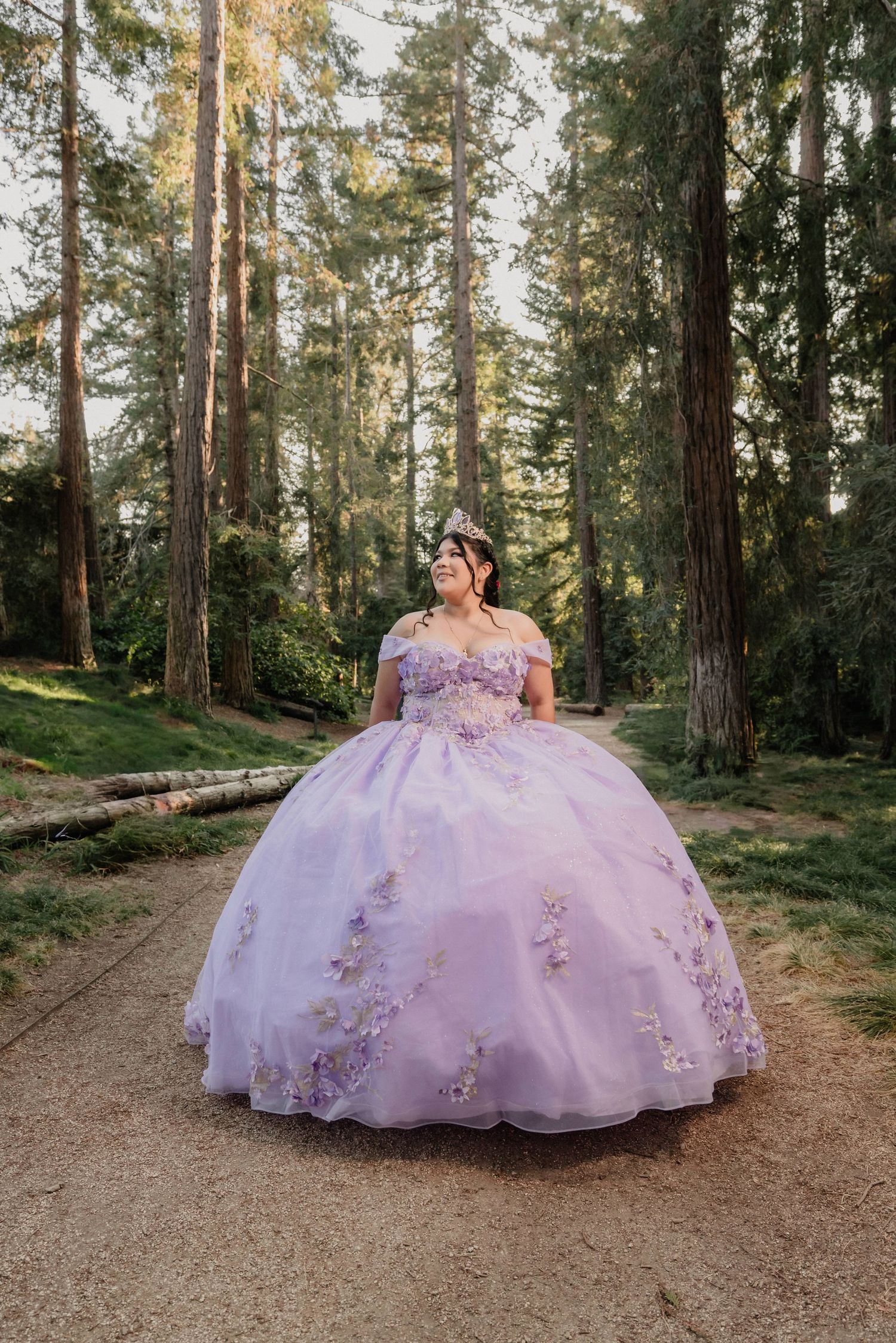 A lavender quinceañera gown with floral details sparkles in a serene redwood forest setting at sunset.