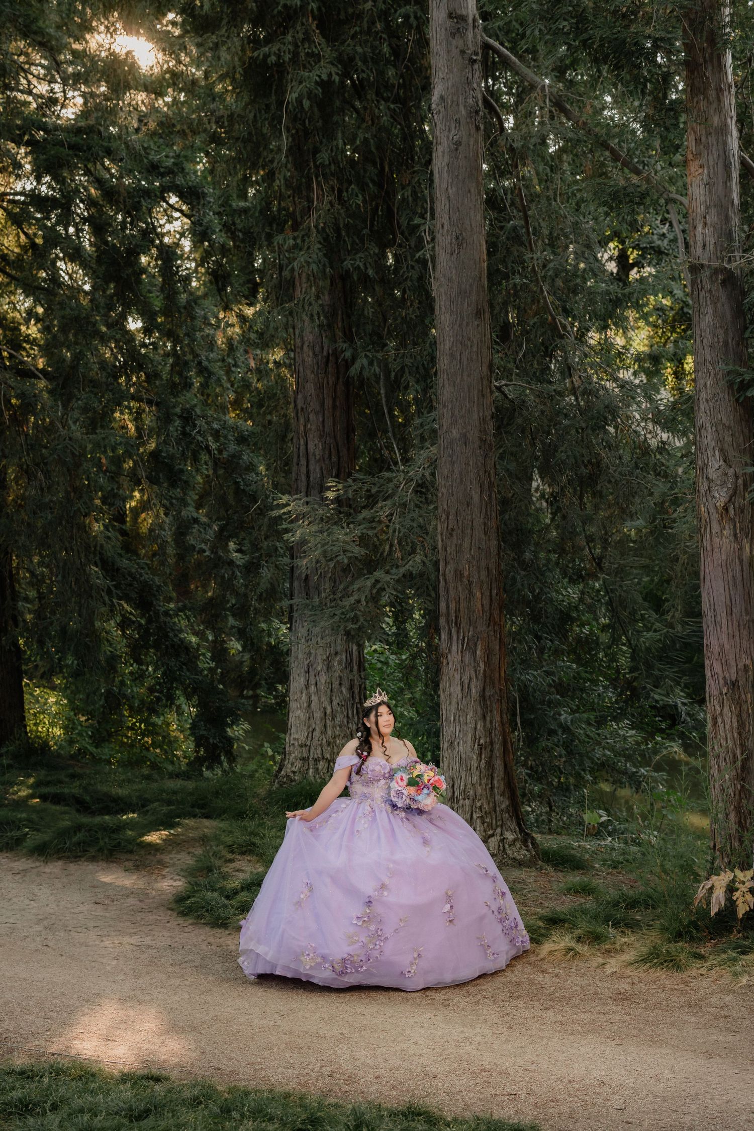 A beautiful quinceanera dress glows in ethereal lavender against a wooded forest backdrop at sunset.