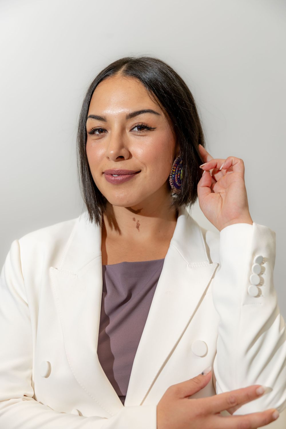 A woman in a white blazer with purple earrings smiling in a professional headshot portrait.