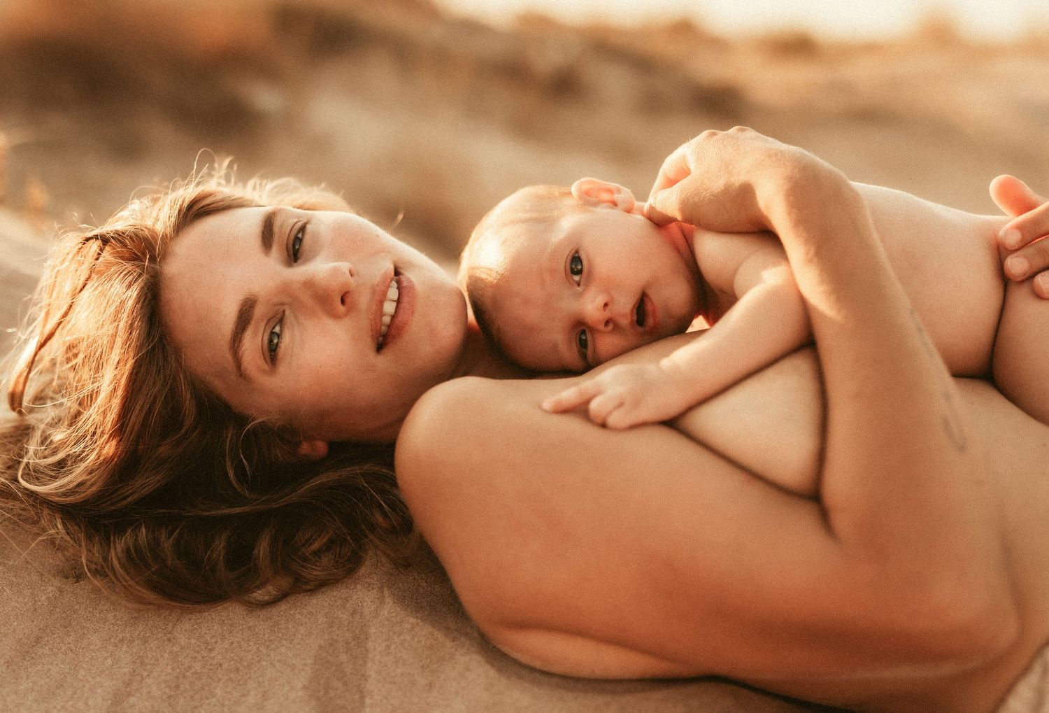 A parent and baby share a tender moment together while lying down in warm lighting. Photographer Javea