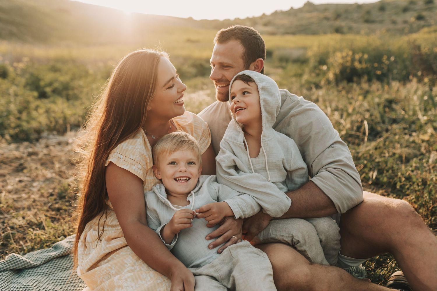 Family enjoying a warm sunset together in a meadow wearing coordinated casual outfits in light blue and grey tones.