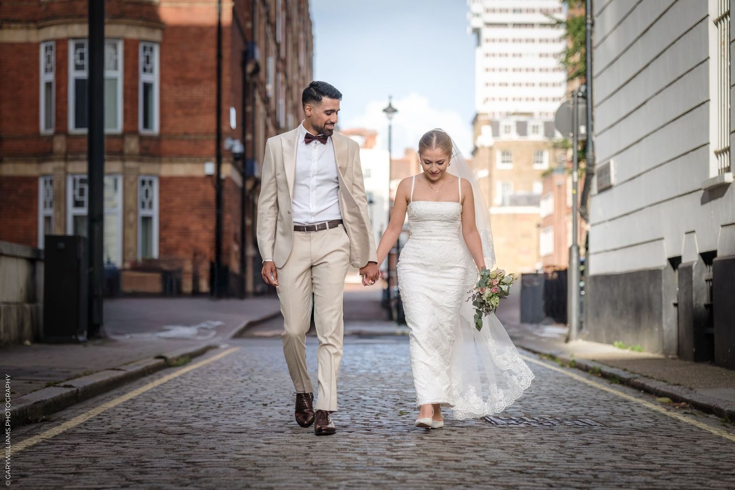 A bride and groom walk romantically down a historic brick street during a wedding photo shoot.