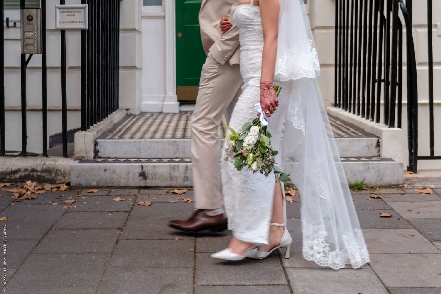 Close-up view of wedding shoes and dress hems as bride and groom stand together on a sidewalk.