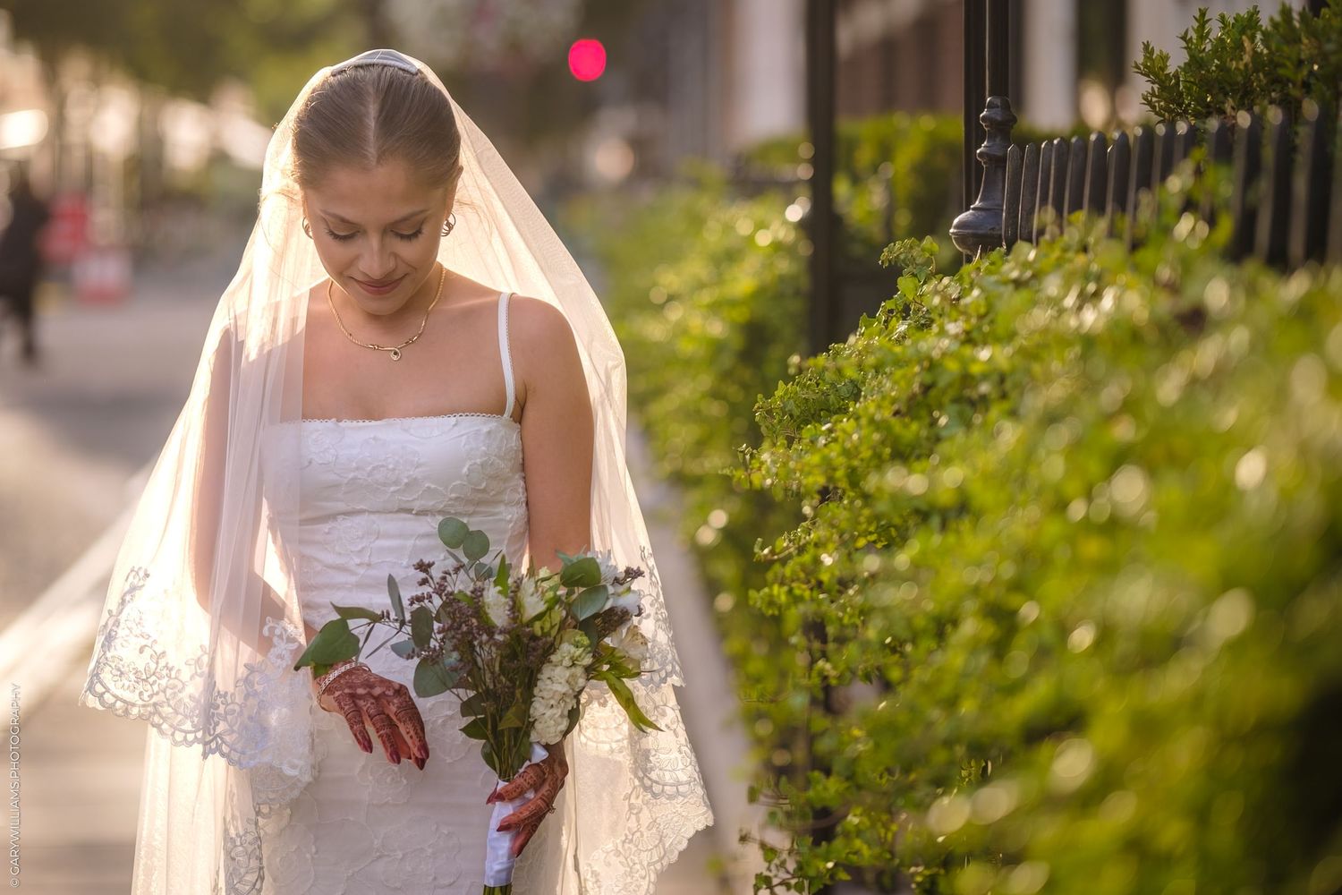 A bride in a white wedding dress holds a bouquet while walking through a lush garden setting during sunset.