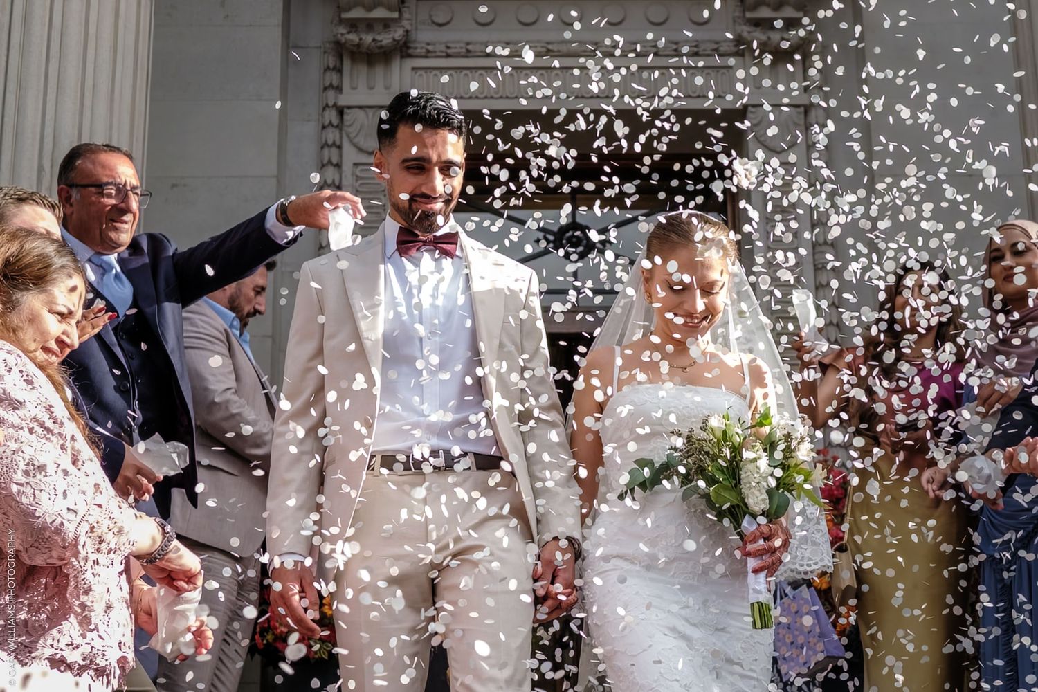 A joyful celebration with confetti and rice being thrown outside at a traditional wedding ceremony.
