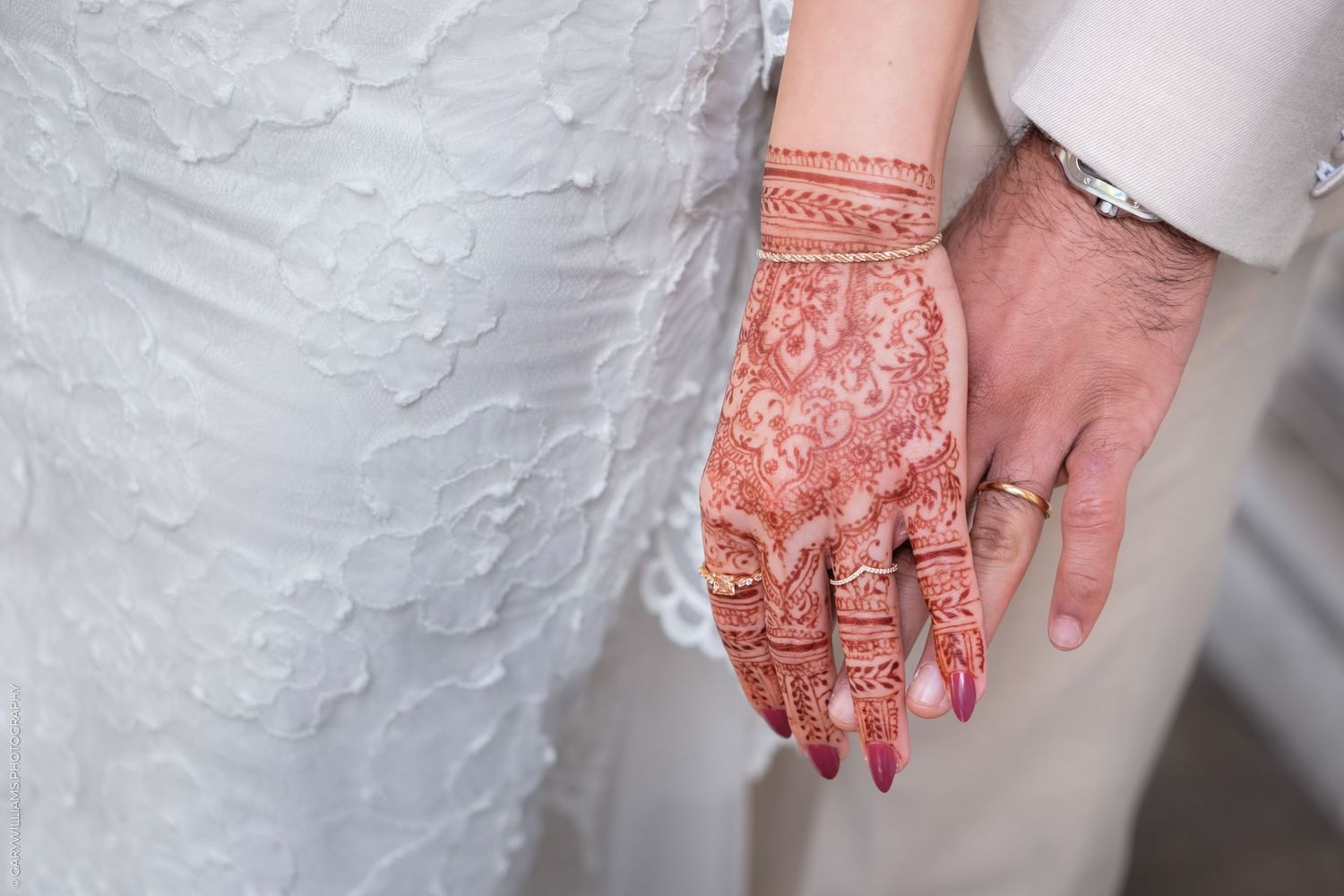 Beautiful intricate henna mehndi design adorns a bride's hand alongside a white wedding dress.