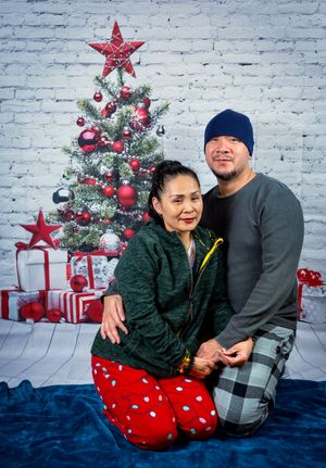 Couple in winter pajamas posing together in front of a decorated Christmas tree for a festive holiday photo session.
