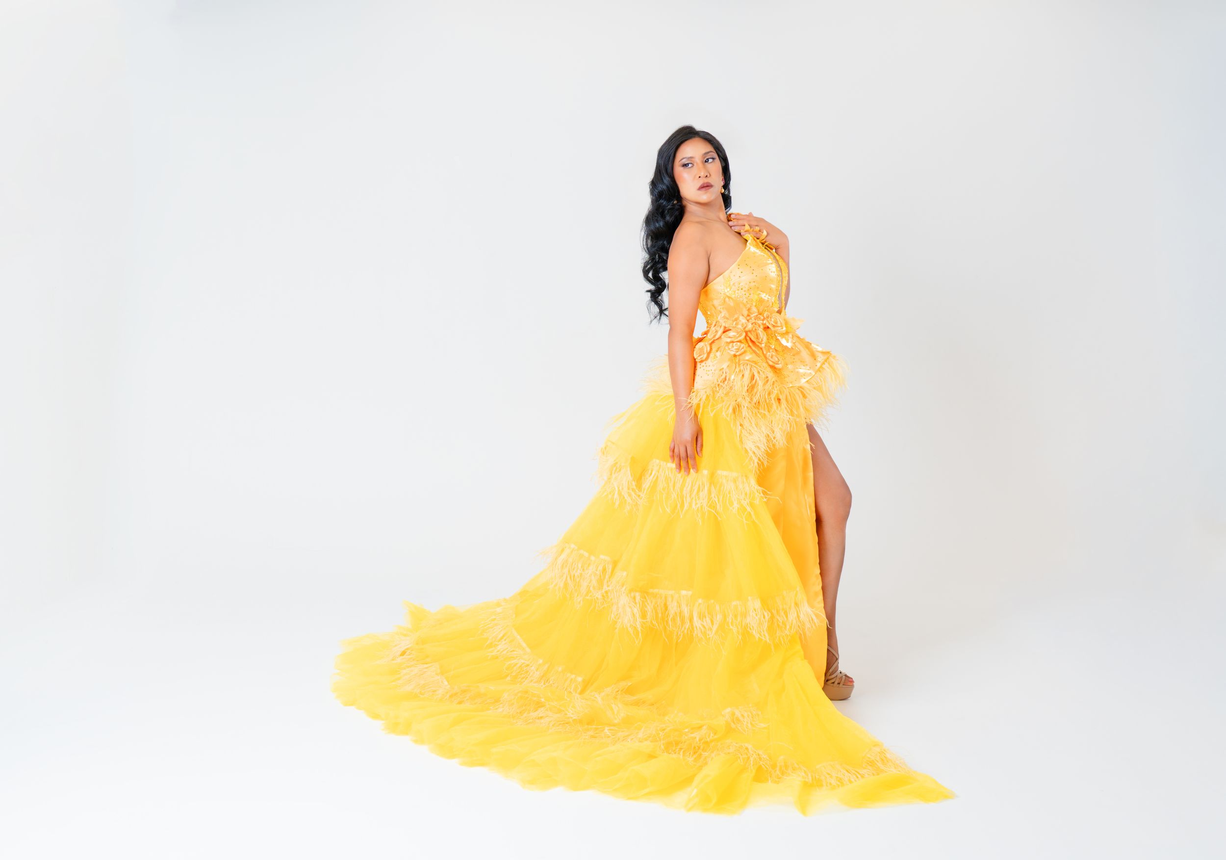 Full-length view of a model posing in a luxurious yellow feathered gown with a sweeping train in a studio photoshoot.