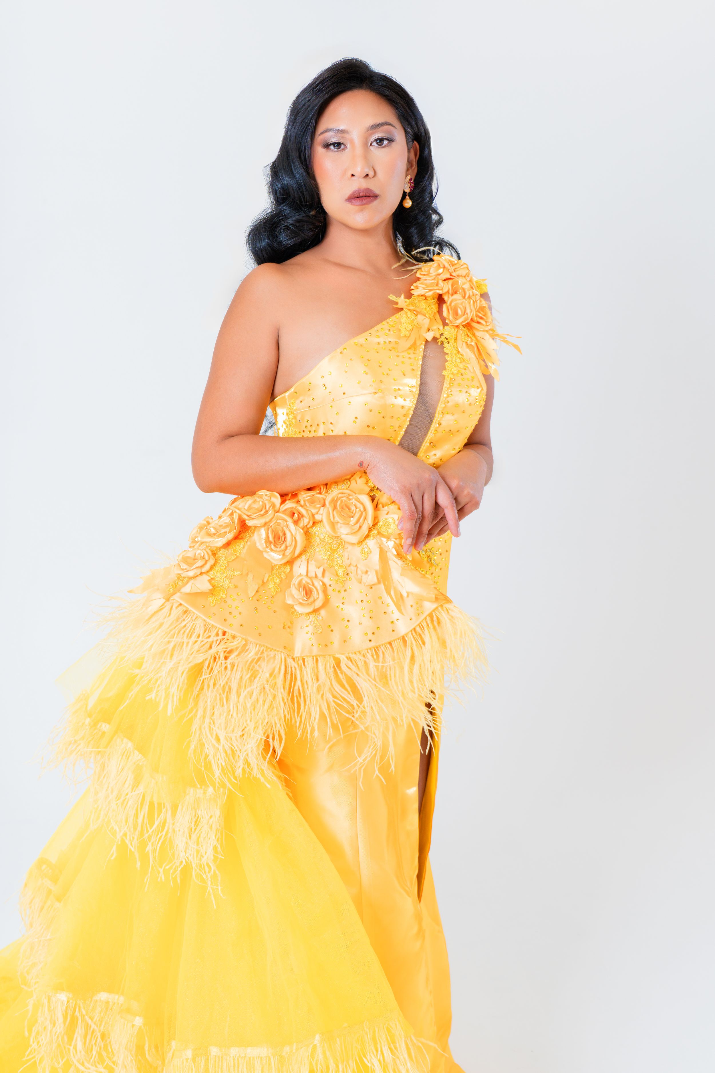 Close-up portrait of a model wearing a yellow couture gown with floral and feather details during a studio fashion shoot.