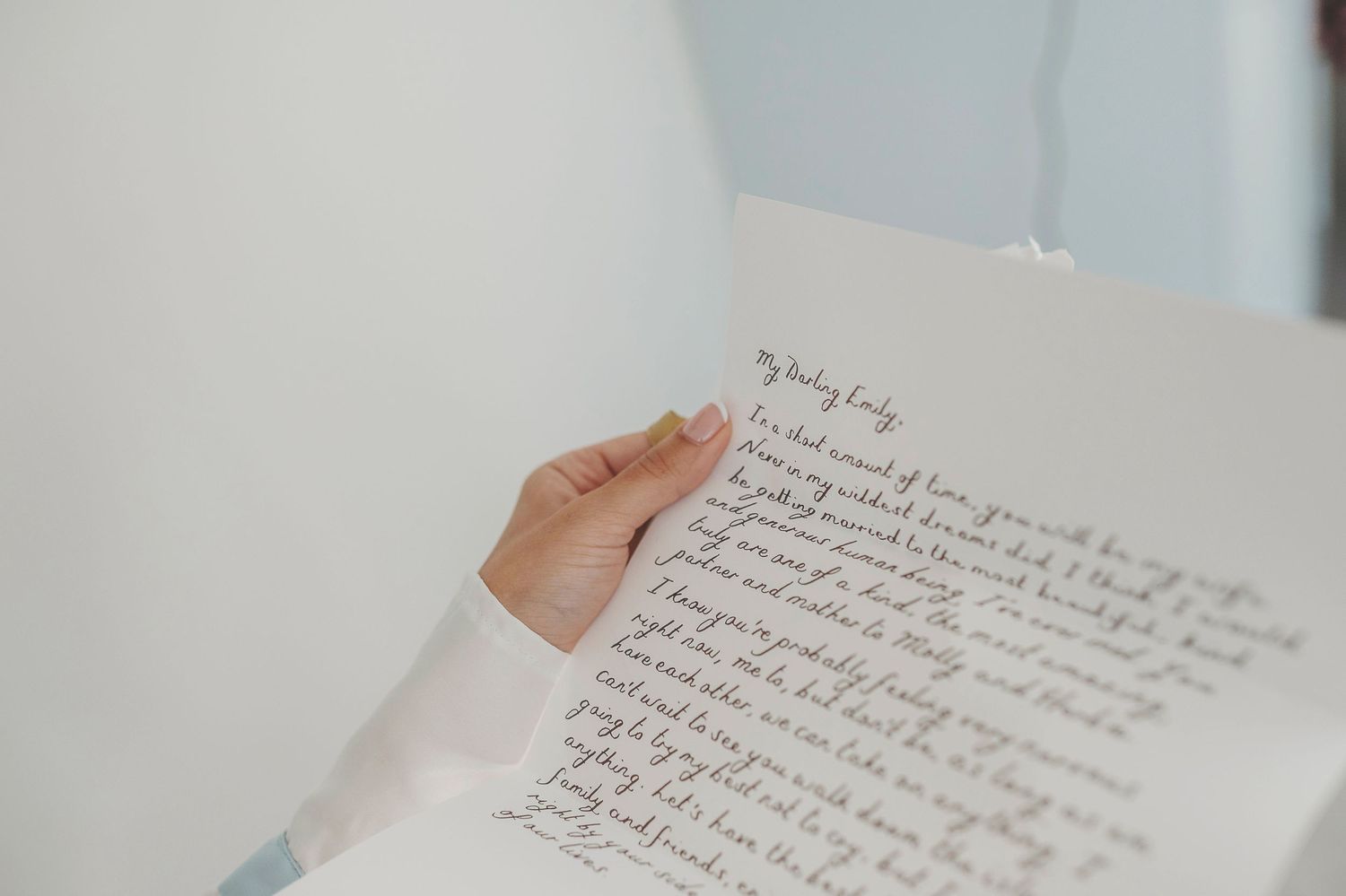 Close-up view of handwritten text on a white page with fingertips holding its corner.