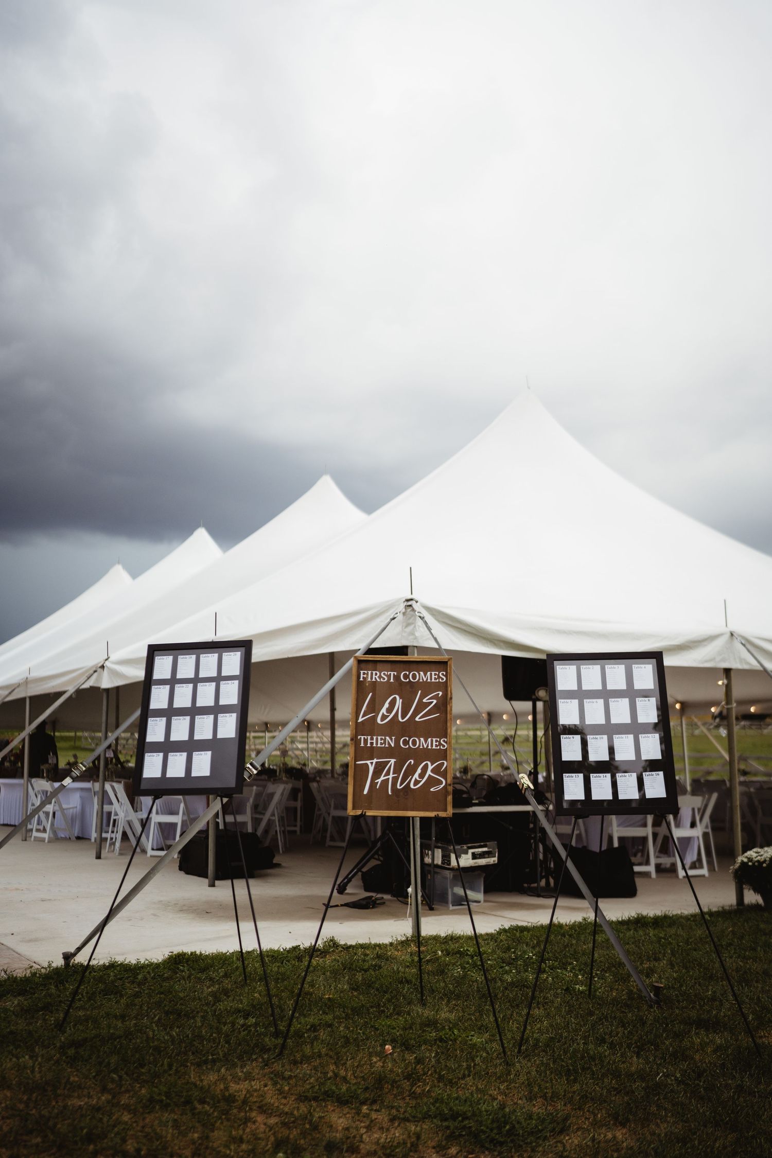 White wedding tents set up on a grassy field under overcast skies with a rustic wooden sign.