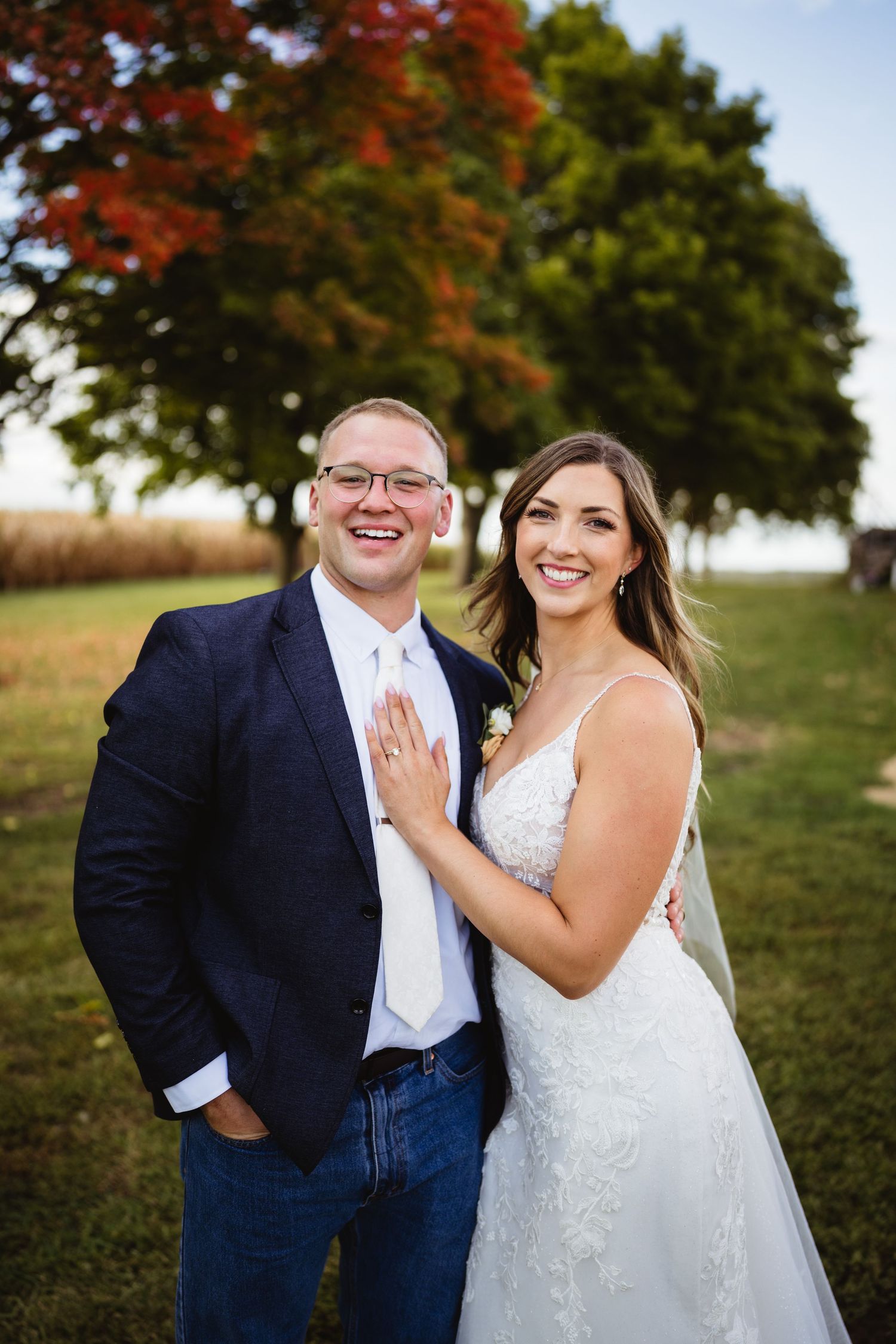A couple in wedding attire sharing joyful moments against autumn trees during an outdoor photography session.