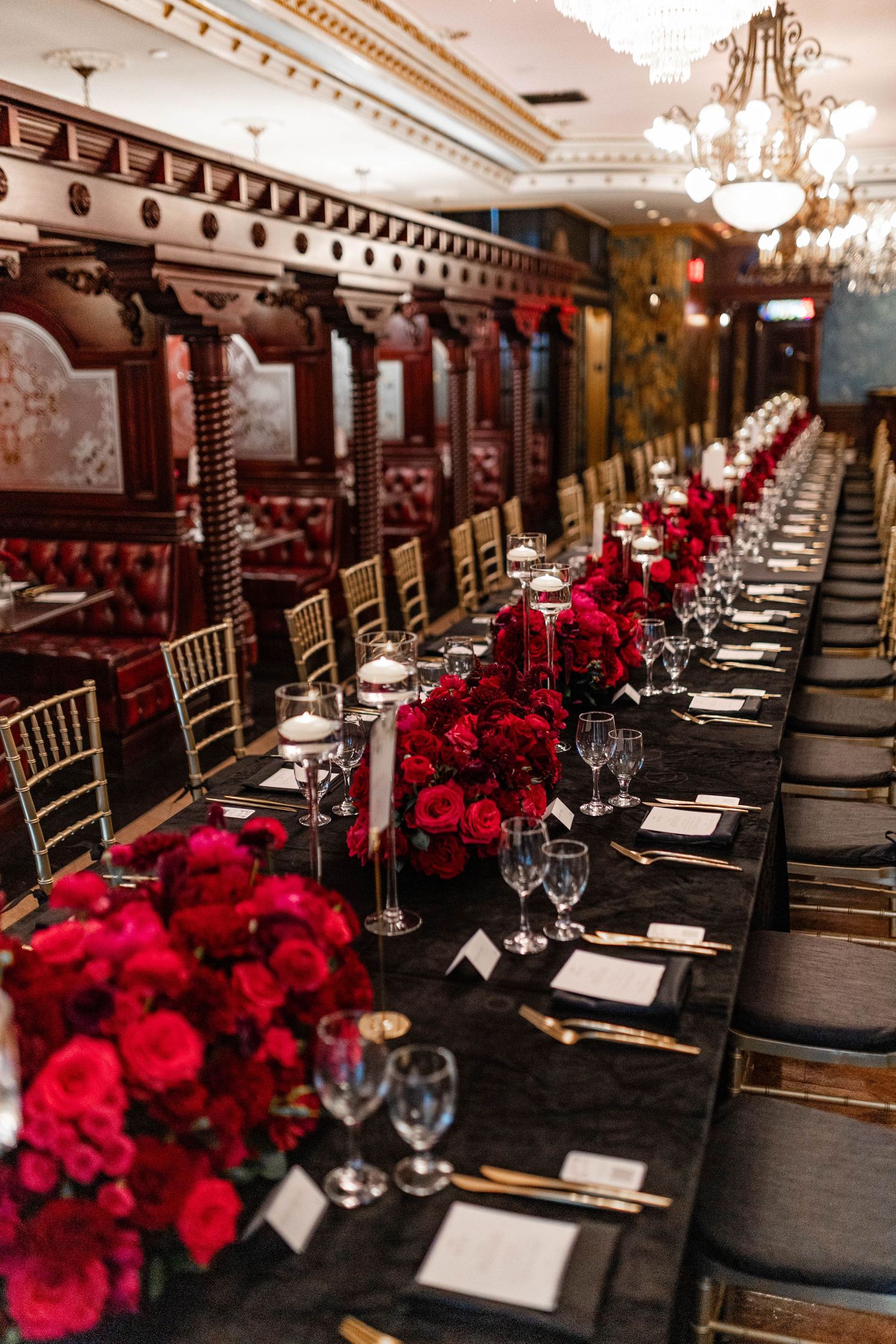 Elegant wedding reception table decorated with dark chairs, crystal glassware, and vibrant red rose centerpieces.