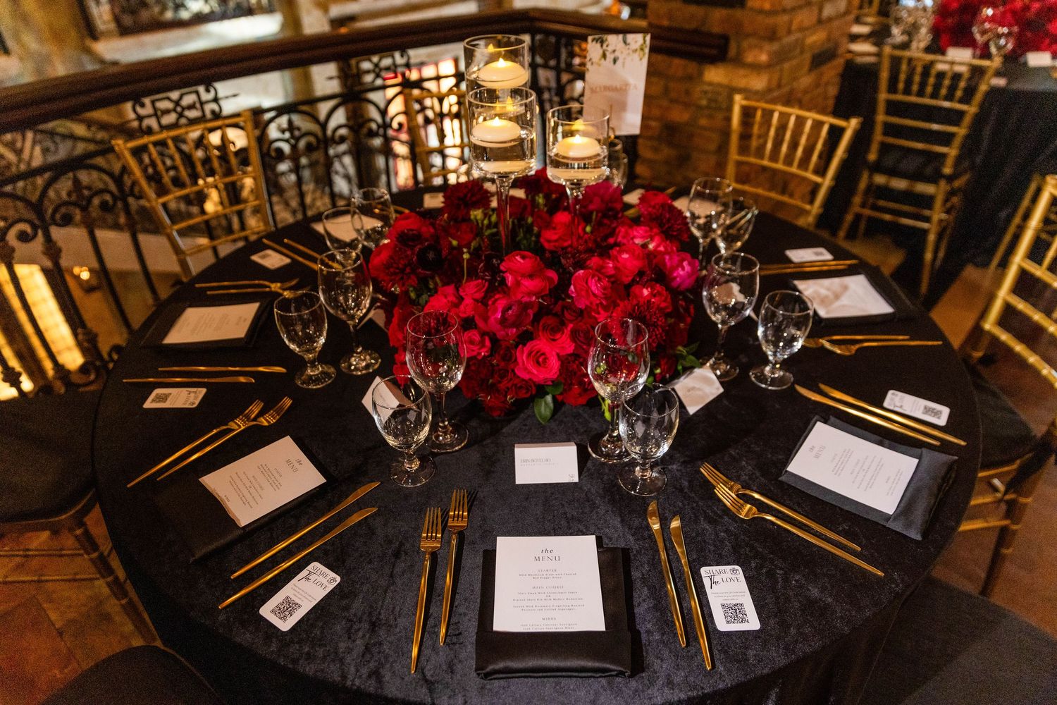 Round banquet tables with gold chiavari chairs and dramatic red floral centerpieces at a wedding reception.