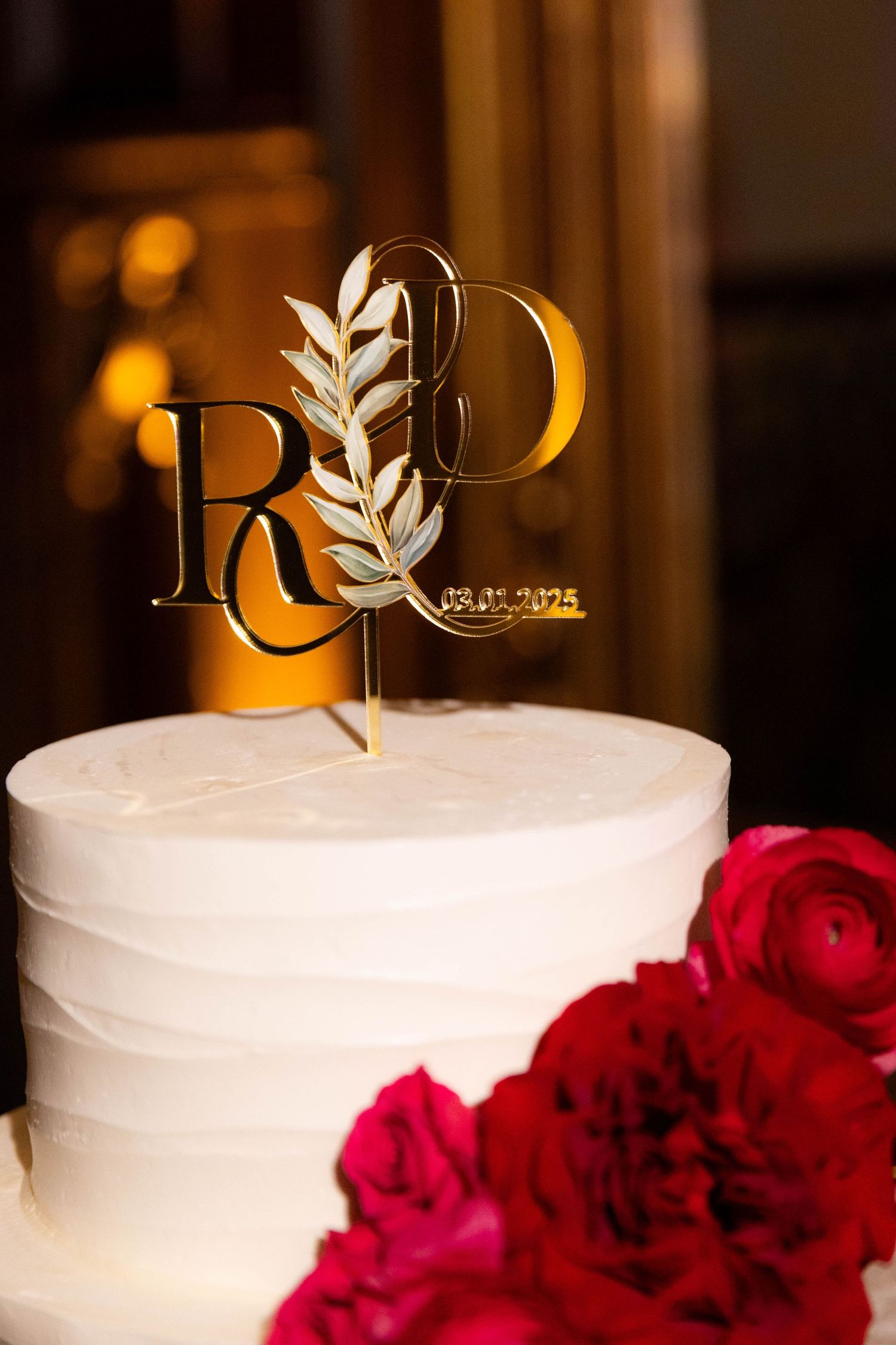 Elegant wedding cake topped with metallic accents and red roses on white fondant.
