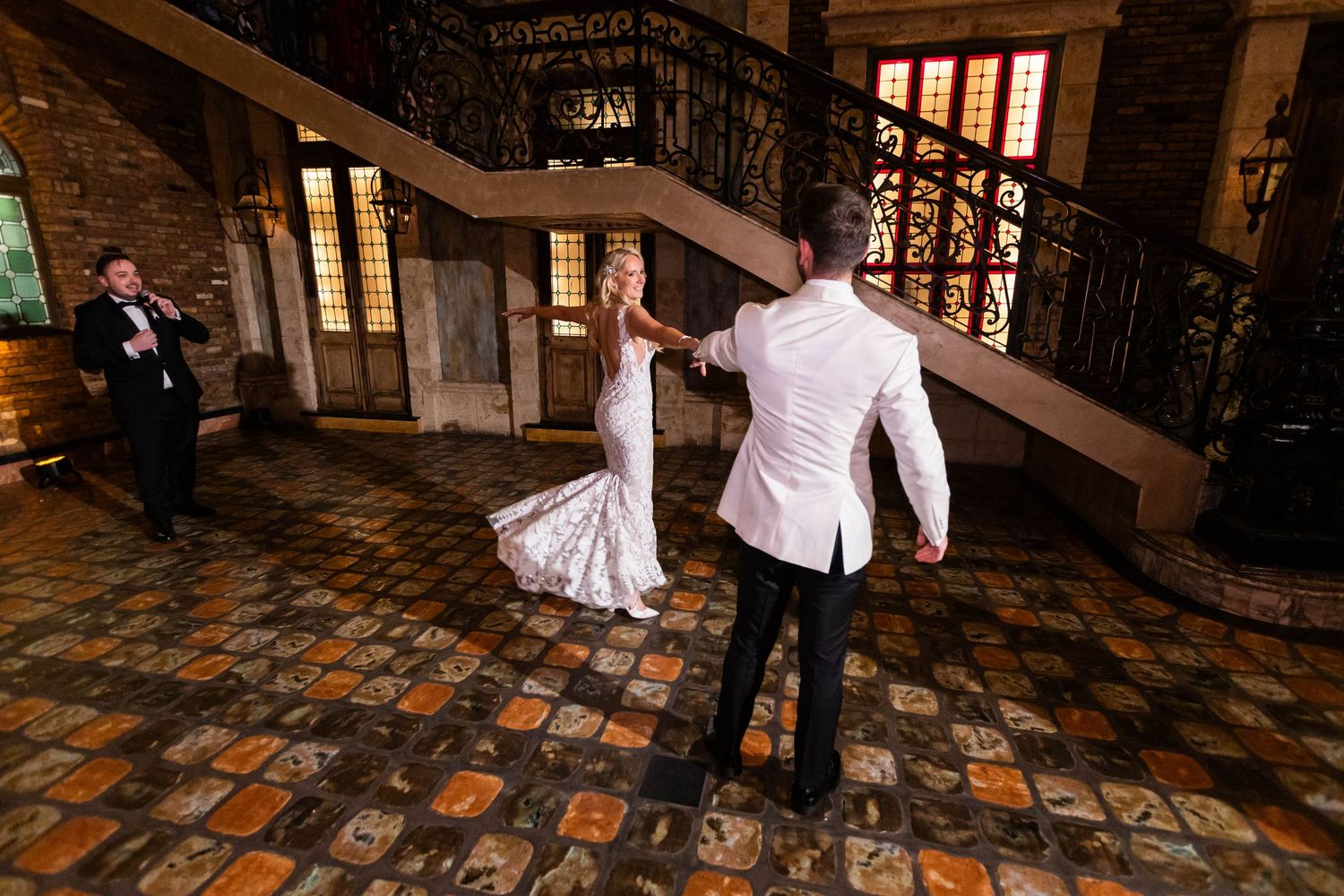 Couple dancing on a vintage patterned floor in an ornate stone-walled venue with ambient lighting.