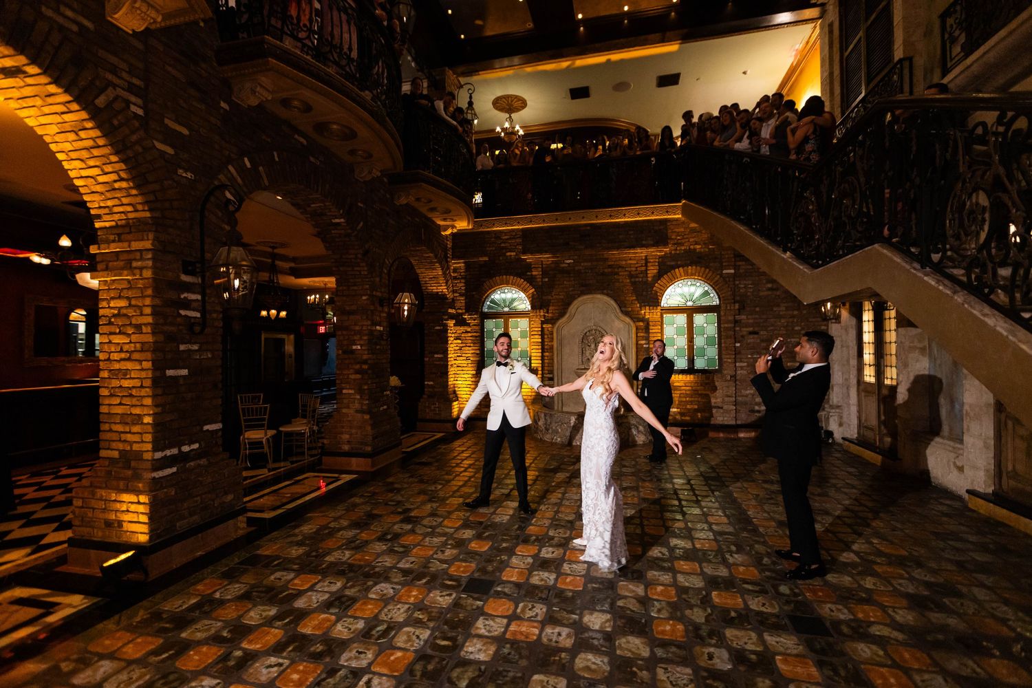 Wedding guests take their seats in an elegant brick-walled venue with decorative lighting.