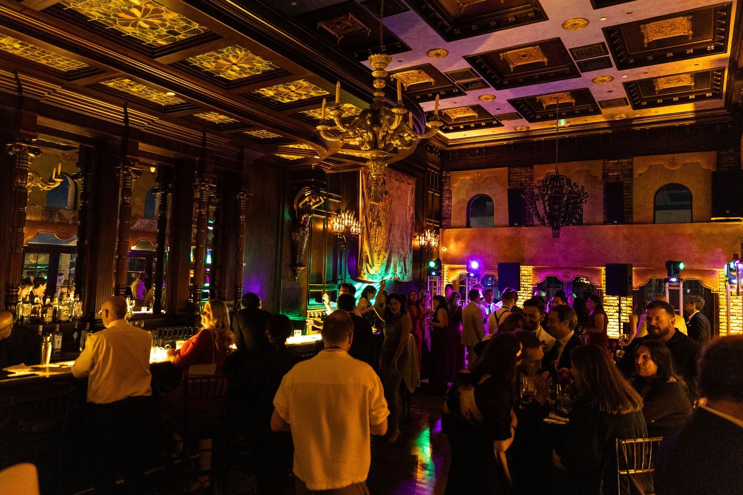 Wedding guests dancing and celebrating on a dark dance floor with colorful mood lighting.