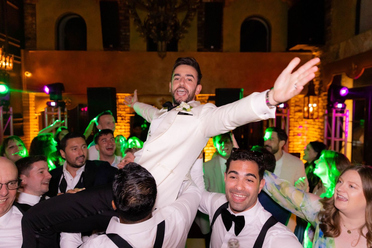 Lively dance floor scene with celebratory guests surrounded by festive lighting and decor.