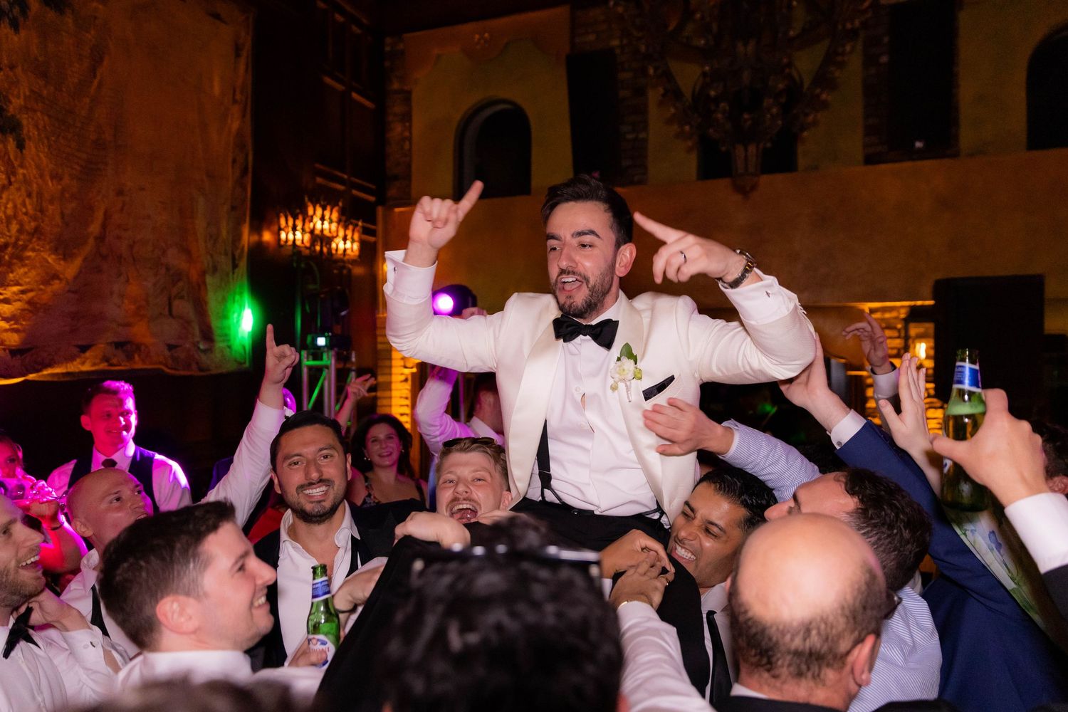 Wedding party dancing and celebrating during reception party with colorful lighting effects.