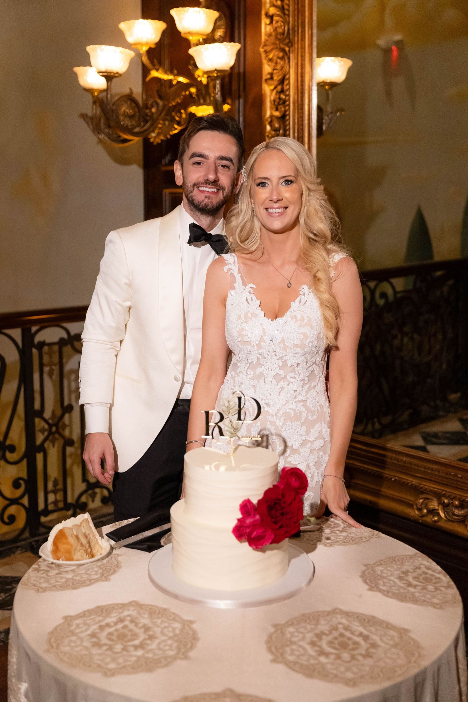 Bride and groom cut their elegant white wedding cake together at an ornate reception venue.