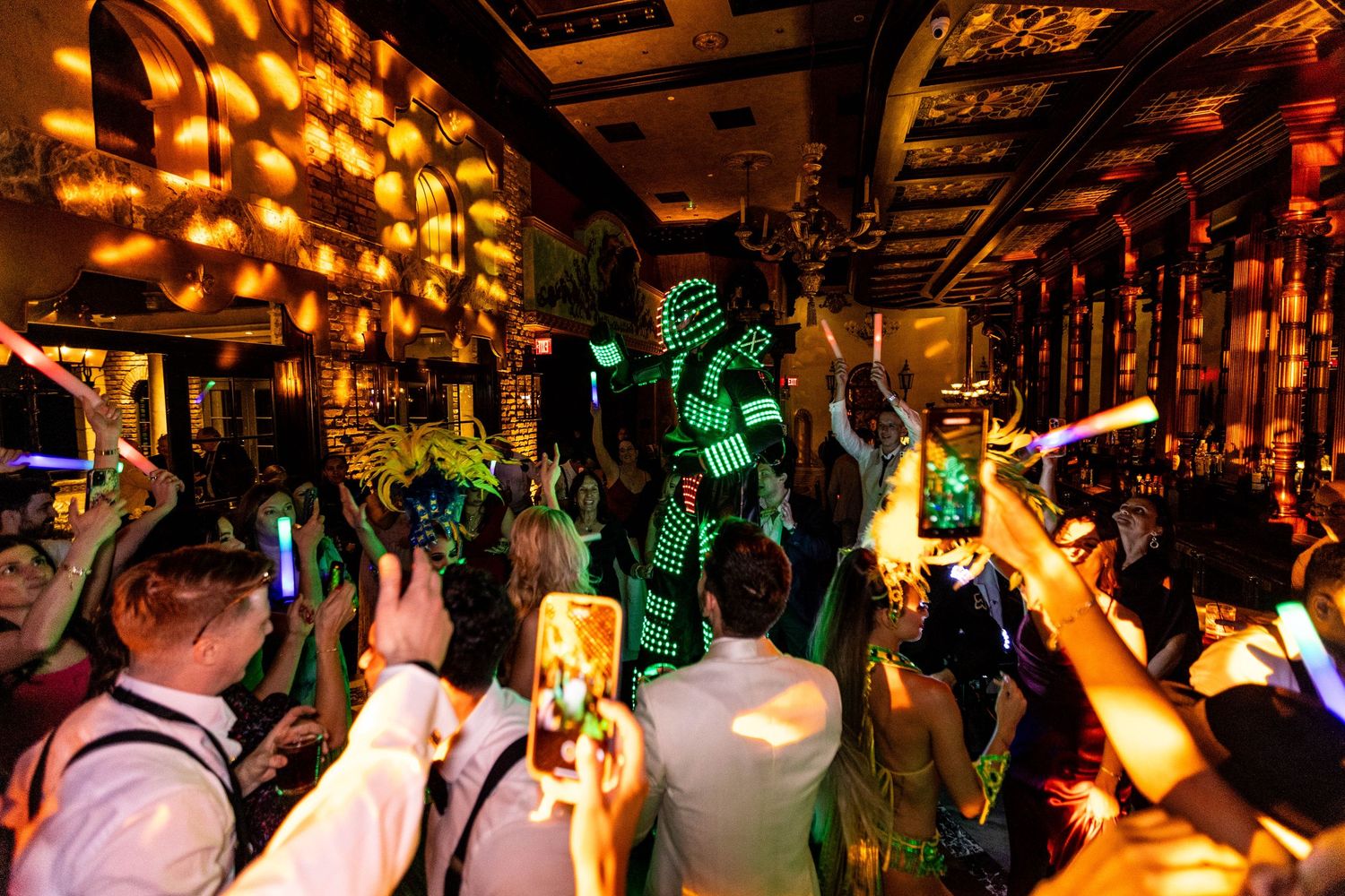 Amber-lit ballroom filled with party guests dancing under rows of warm overhead lighting.