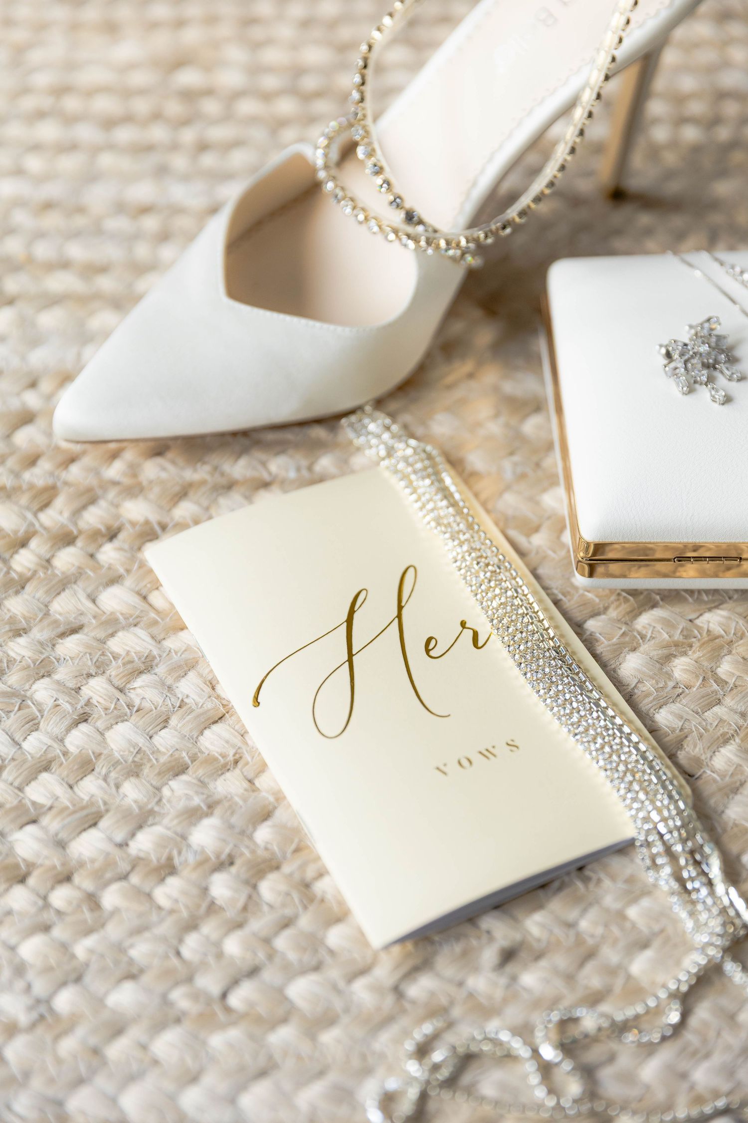 Elegant white bridal shoes and gold wedding stationery arranged on textured fabric.