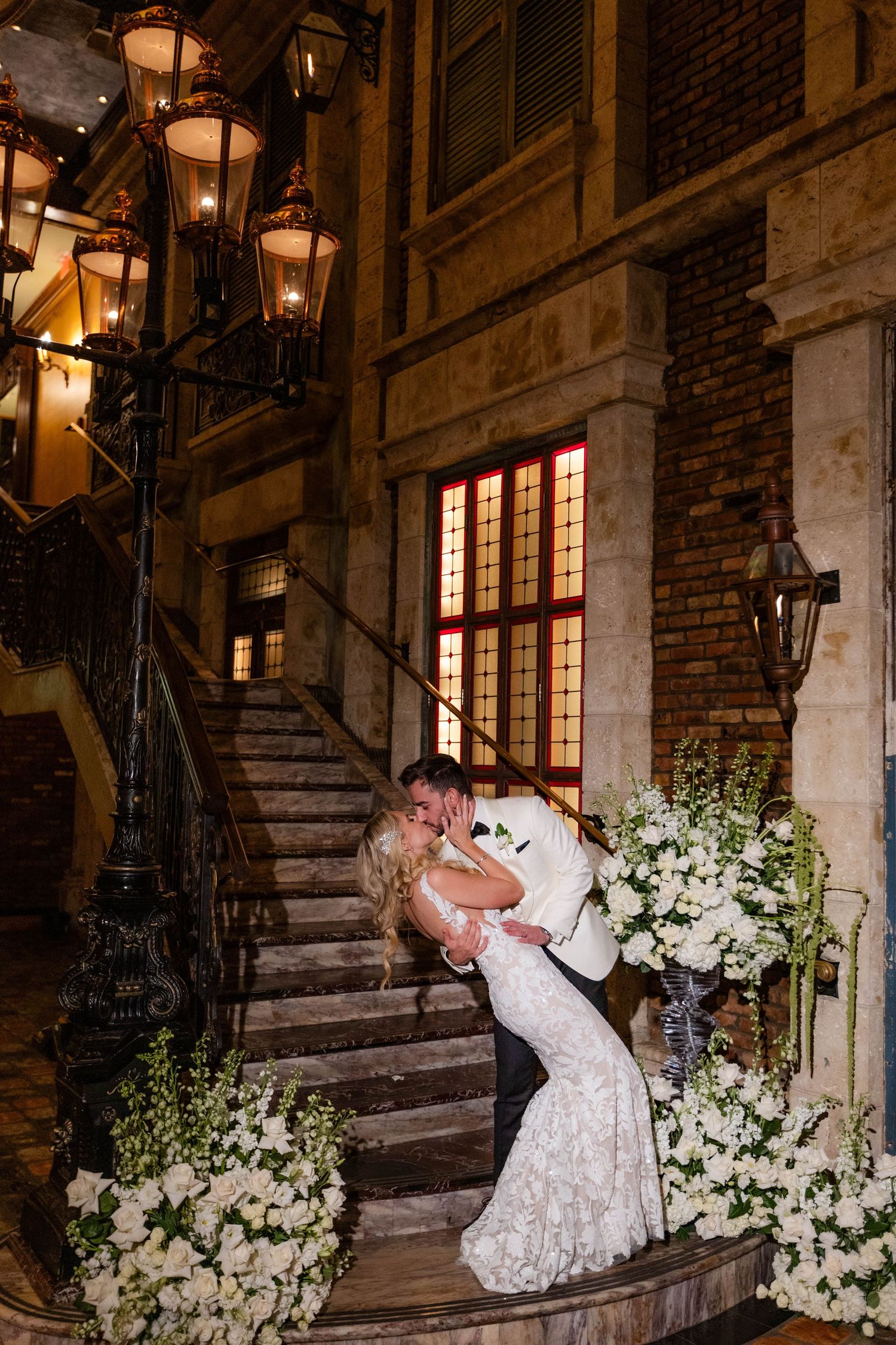 Wedding couple dances near a stone staircase adorned with white floral arrangements.
