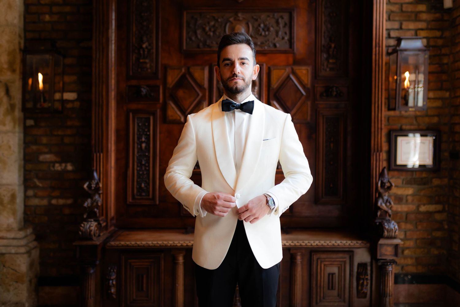 Classic groom portraits in white tuxedo against rustic brick wall background.