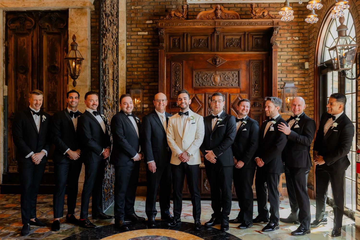 Wedding party lineup in formal attire against a classic brick wall backdrop.