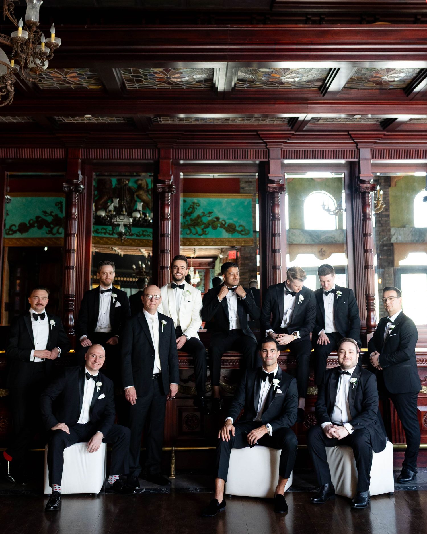 Groomsmen in black tuxedos gathered in an elegant wood-paneled room.