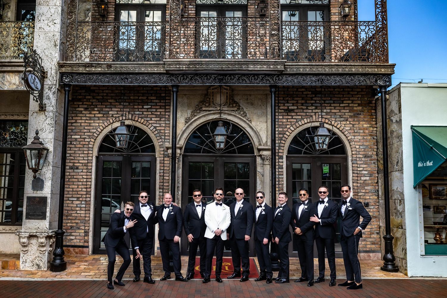 Groomsmen in dark suits posed in front of historic brick building facade.