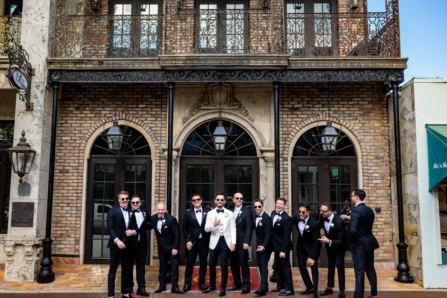 Wedding party posing outside brick building with classic architecture and arched windows.