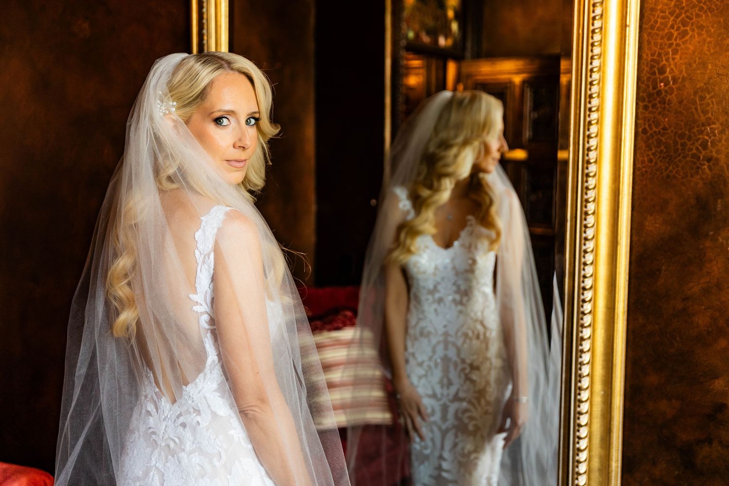 Bride in white lace gown reflected in vintage gold framed mirror.