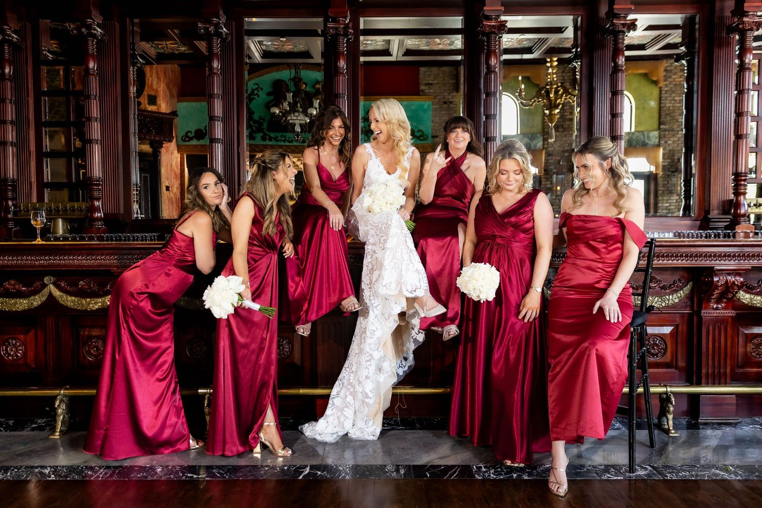 Wedding party in burgundy bridesmaid dresses posing in a rustic brick venue.