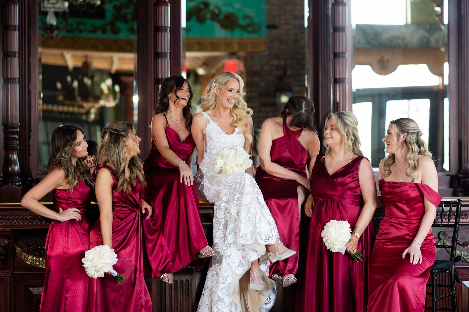 Bridal party in burgundy dresses poses with bride in white lace gown.