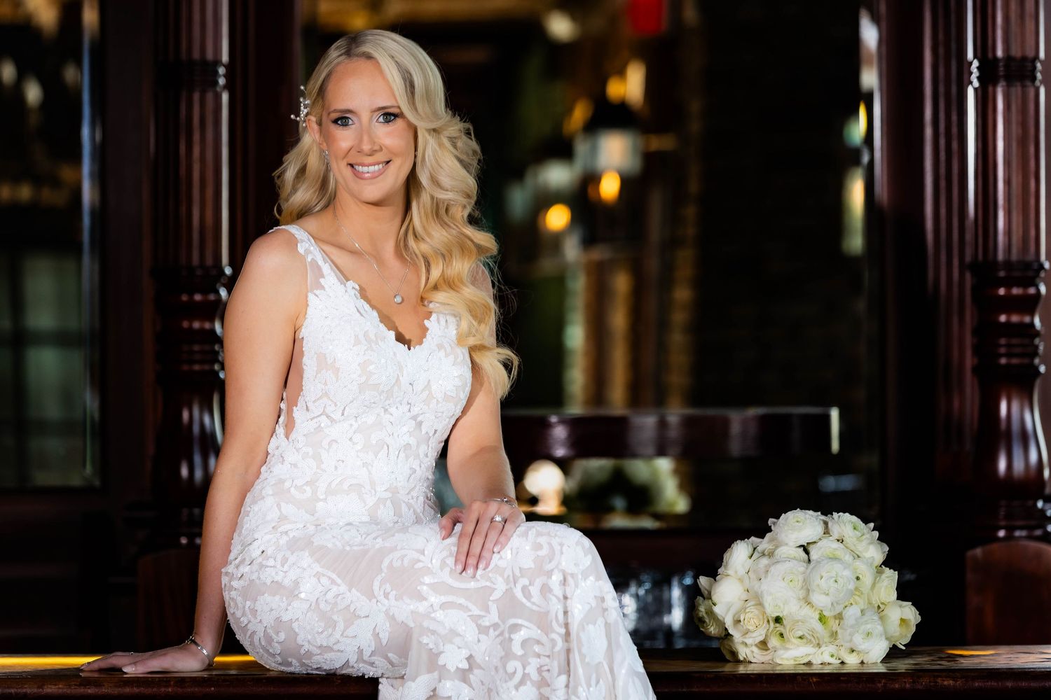 Bride wearing white lace wedding dress poses in vintage-style indoor setting.