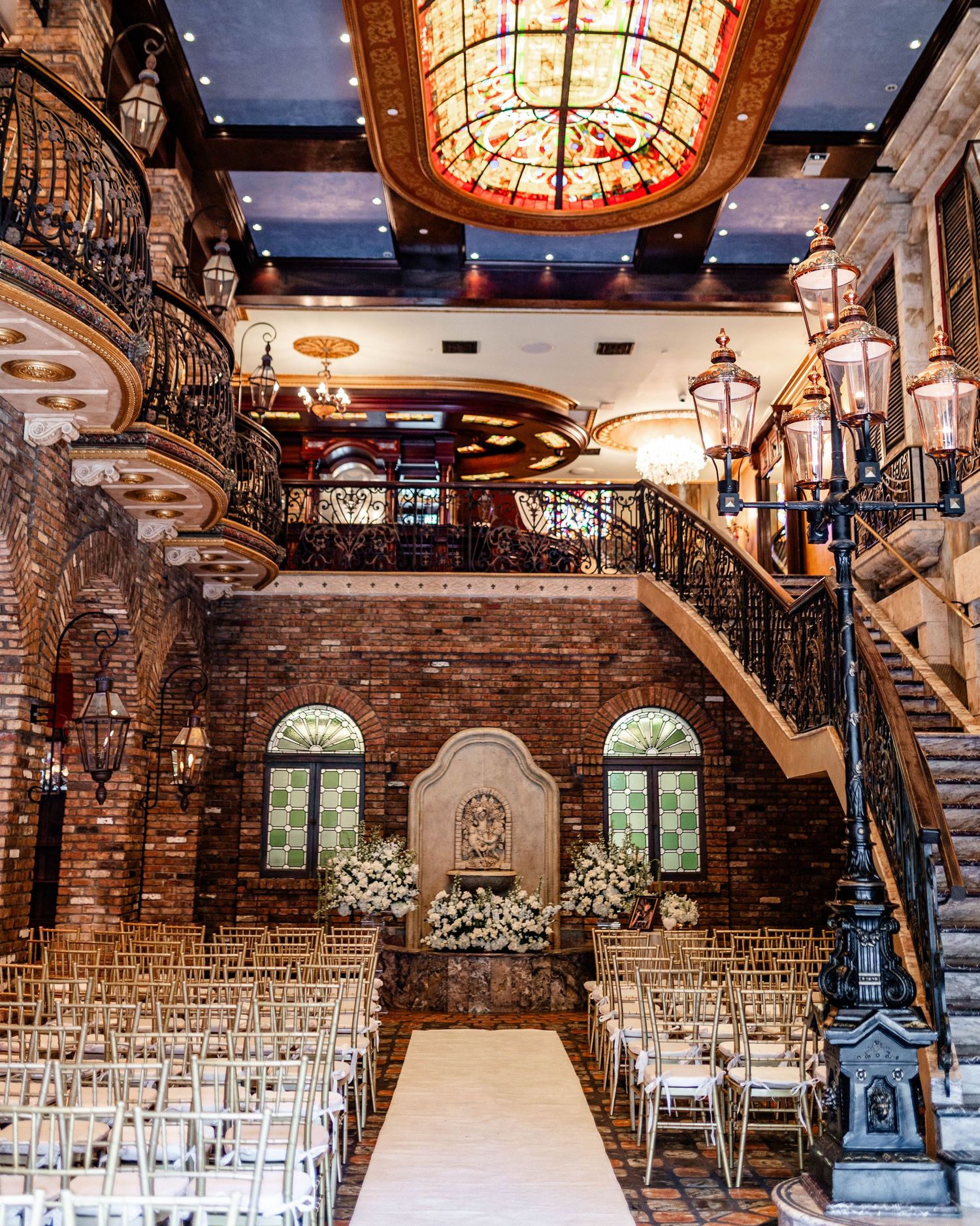 Wide view of an elegant wedding venue with exposed brick, crystal chandeliers and white ceremony chairs.