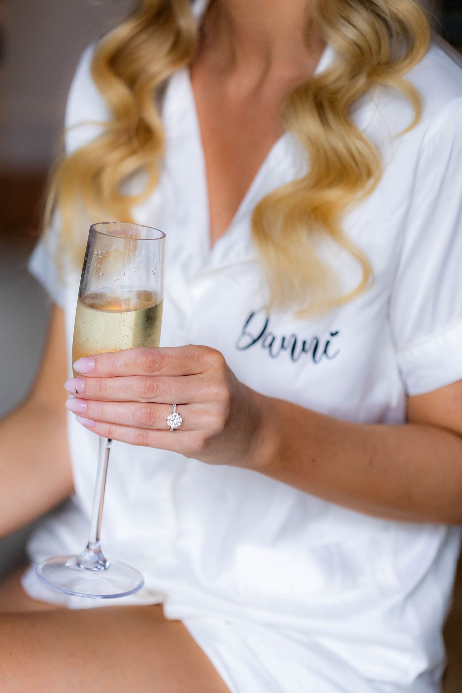 Close up of champagne glass held by person wearing white robe with embroidered detail.