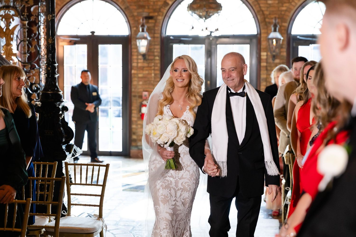 Wedding celebration inside an elegant venue with brick archways and crystal chandeliers.
