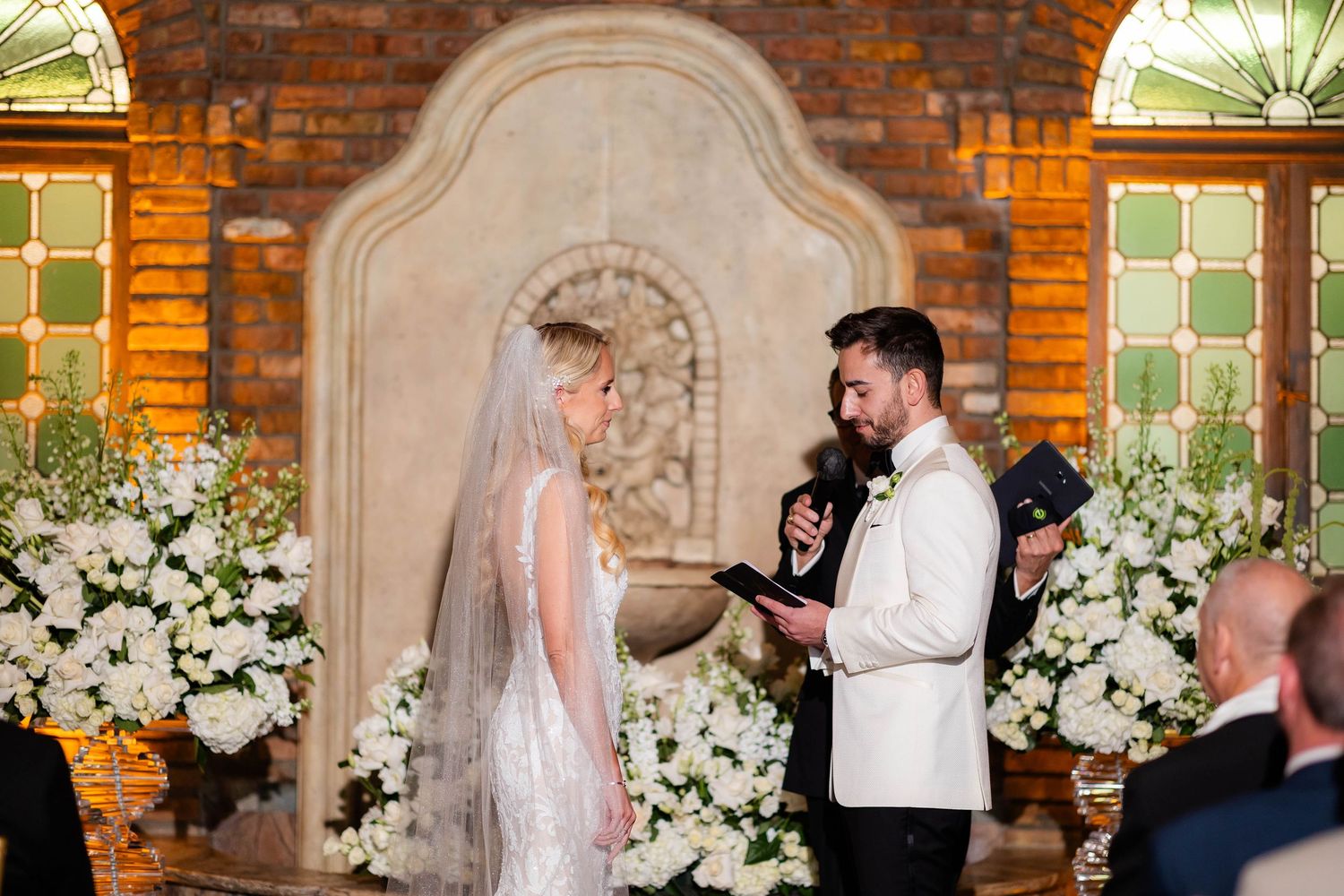Wedding reception setup with white floral arrangements against exposed brick walls.