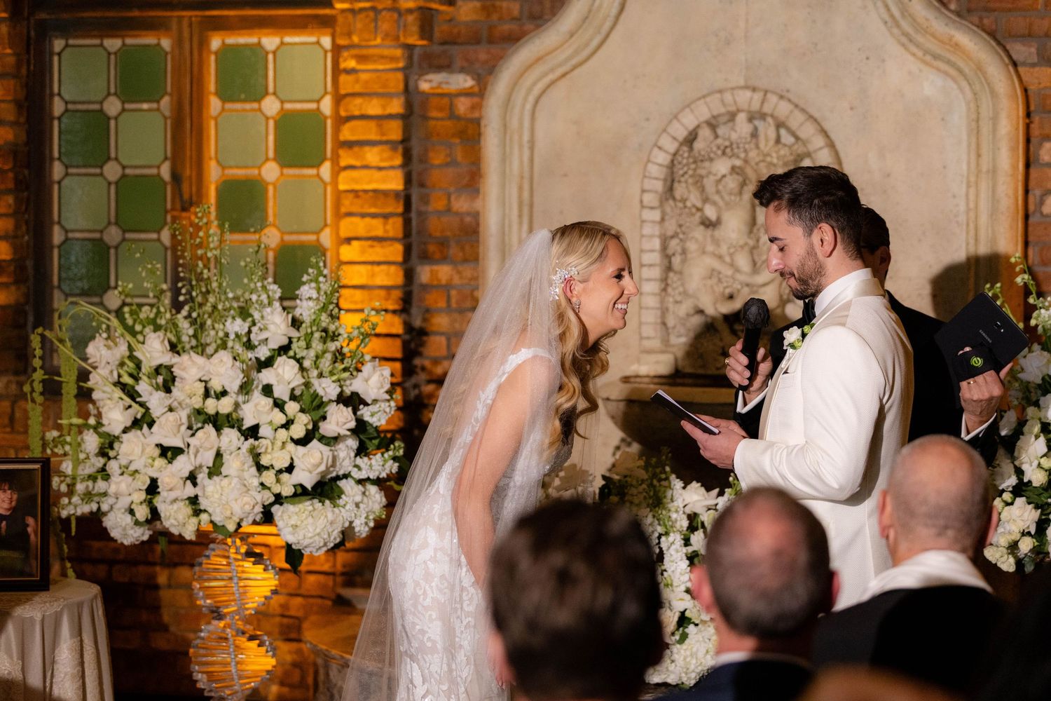Interior of a rustic brick venue with green shutters and white floral decorations.